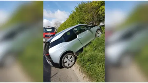 AnnMarie Newbigin A large grey car on the verge of a roadside, it has crashed.