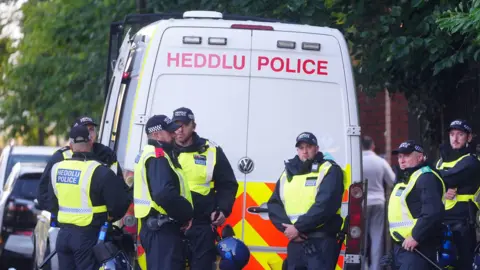 PA Media A group of police officers stood in front of a van that says "Heddlu Police" in capital letters