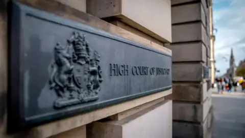 A sign for the High Court of Justiciary on a brick wall in Edinburgh