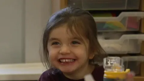 A young girl with brown hair in a ponytail is smiling