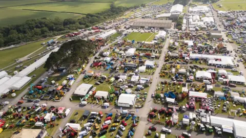 Royal Cornwall Show An aerial photo of the showground, showing lots of vehicles on display, and marquees, laid out on grass with concrete paths