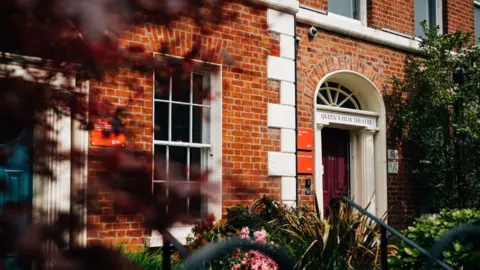 A photo showing the front of the QFT building. The building is a terrace building, with red bricks and white windows. Above the door, Queen's Film Theatre is written in capital letters.