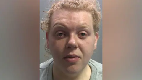 Cumbria Police Hannah Smaile has large eye bags and looks dazed. She has ginger curly hair tied back and is wearing a grey sweater. 