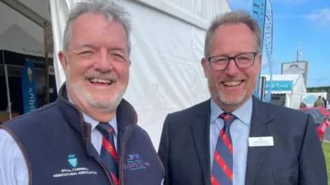 The Royal Cornwall Show's previous secretary and CEO Chris Riddle (left) stood next to Mark Stoddart (right). They are both smiling and looking towards the camera.