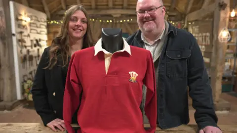 Karen and Lloyd smiling as they stand behind with the repaired jersey