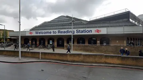 Google The front of Reading railway station, a brick building with a large sign outside reading "welcome to Reading Station". There are people walking outside and bikes locked up by the entrance.