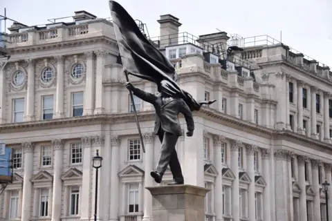 Getty Images A grey statue of a man wearing a suit, marching forward, carrying a flag that covers his face