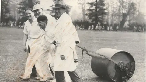 Droitwich Spa Cricket Club Four men pulling cricket pitch roller in black and white photo