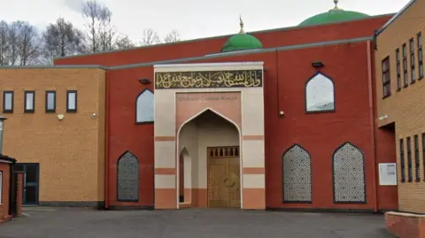 Google The red and sand-coloured brick-built front of Oldham Central Mosque, with arched windows covered in detailed patterns