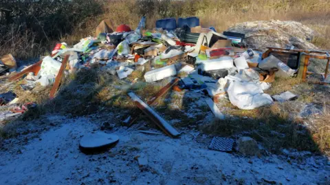 Hertfordshire Constabulary A large amount of rubbish lying on the ground, there is snow in front of it, and grass all around it. The items include a chair, boxes, broken items and wood. 