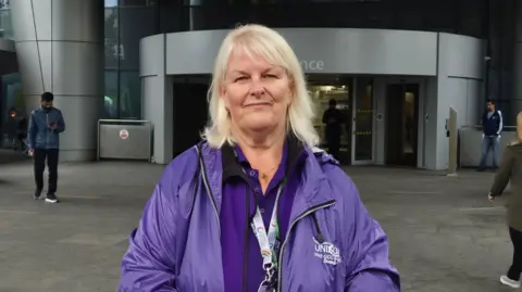 A woman wearing a purple jacket with Unison written on it, standing in front of a hospital building