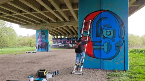 Tony Nero Blue artwork being painted on pillars under a flyover.