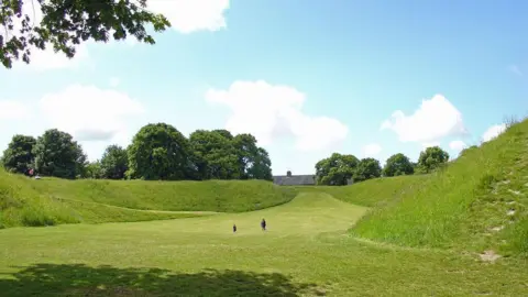 Dylan Moore Maumbury Rings earthworks - a large grass bowl-shaped area surrounded by trees