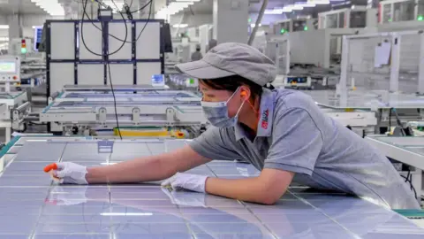 A woman leans over a large sheet of solar panel modules at a factory in Jinhua, Zhejiang Province of China. 