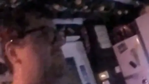 Close up of Bennett's face while he is stood in a dark kitchen