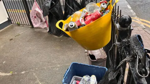 Phil Harrison/BBC Rubbish bags and buckets hung on a fence.