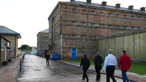 Four people walking towards Barlinnie Prison, with what appears to be a prison officer walking the other way towards them