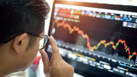 Man wearing glasses looking at a slightly blurred screen showing a stock price chart