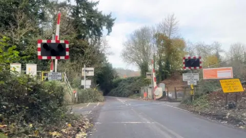Network Rail The level crossing at Burrows Lane, where the road runs over the railway. The gates are open in the picture.