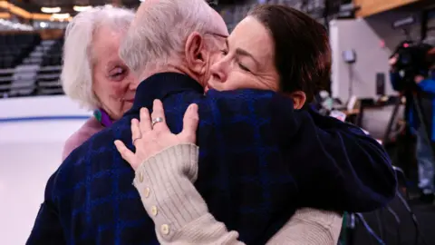 Getty Images Nancy Kerrigan hugging man in black and blue shirt next to ice rink