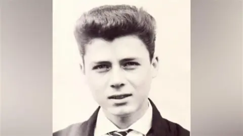 Alan Florence Alan Florence aged 17 in 1961, he has dark hair in a quiff style and a white shirt with stripped tie and black jacket, the photo is in black and white, a white background is behind him.