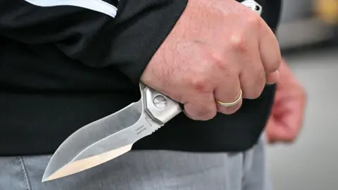 A man, wearing a gold ring, is holding a knife. 