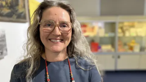 Councillor Marina Strinkovsky smiling with large rectangular glasses, below shoulder length wavy hair and a multi-coloured beaded necklace
