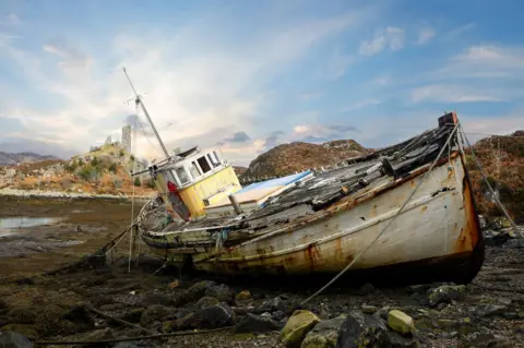 Cath Stanley Rusty boat tilted on its side, berthed on a rocky beach