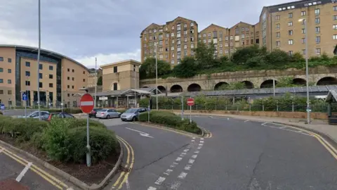 A car park outside a railway station with railway tunnels and buildings in the background