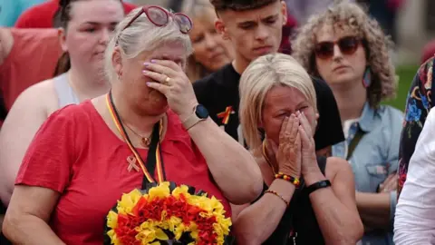 Two women, part of a group who held a minute's silence in May 2024  in memory of people who died because of the infected blood scandal. They are covering their faces with their hands in grief. 