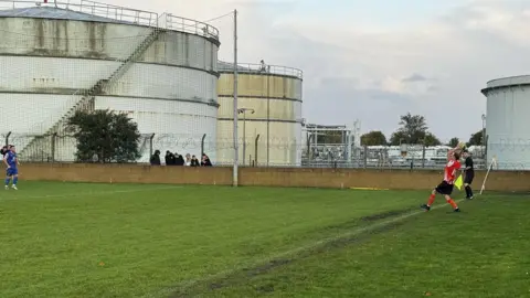 Paul Gully A player takes a throw in on the side of the pitch with oil storage towers visible in the background