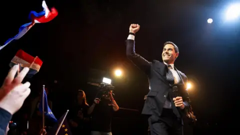 EPA Rob Jetten stands on a podium and is greeted by supporters.