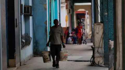  man carries paint buckets with water ahead of an announcement by Cuba's grid operator UNE that it had reconnected most of the country to the national grid, though millions remained without power as the country struggles to generate even one-third of current demand amid an ongoing U.S. fuel blockade, in Havana, Cuba, July 7, 2026. R man carries paint buckets with water ahead of an announcement by Cuba's grid operator UNE that it had reconnected most of the country to the national grid, though millions remained without power as the country struggles to generate even one-third of current demand amid an ongoing U.S. fuel blockade, in Havana, Cuba, July 7, 2026. REUTERS/Norlys Perez
