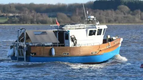National Crime Agency A small blue, white and wooden fishing boat on the sea.
