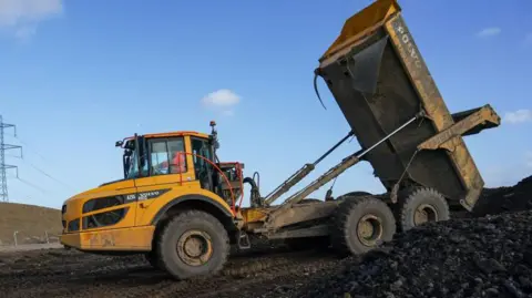 A yellow forklift tipping construction waste onto a mound.