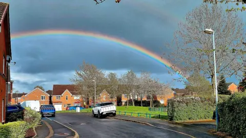 Ian Yates A double rainbow on a cloudy sky can be seen over houses and cars.