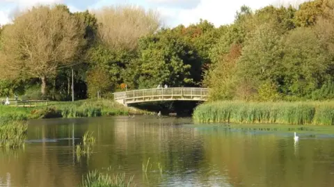 Paul Bryan/ Geograph A nature reserve with water underneath a wooden bridge- surrounded by trees

