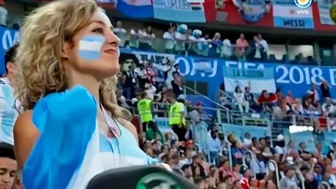 Linda Pontoriero a young female Argentina football supporter with long curly blond hair and the Argentine flag painted on her cheek looks proudly at the pitch from the stands. 
