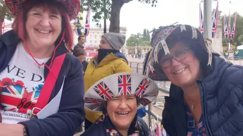 BBC Three women wearing Union Jack celebratory clothing smile on the Mall in London