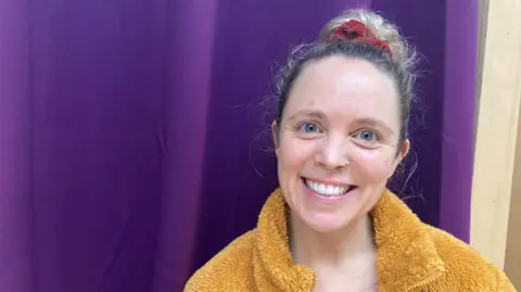 Emma smiles at the camera whilst a yellow fleece.