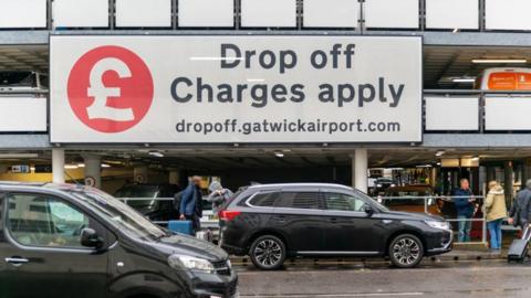 Cars stopping outside Gatwick with a large sign reading "Drop off Charges apply"