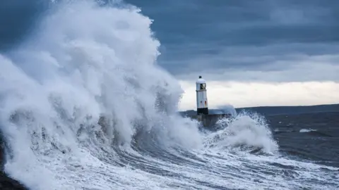 Gary Williams Giant waves seen next to a black and white lighthouse.