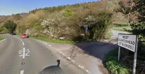 Google maps Google maps street view image of the A39 at West Quantoxhead. The A39 is winding round to the left and to the right a road veers up, with the West Quantoxhead sign at the bottom of the hill. 