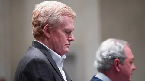 Alex Murdaugh wears a grey suit and a white shirt. He looks down as he hears his guilty verdicts in the trial over his wife and son's death.