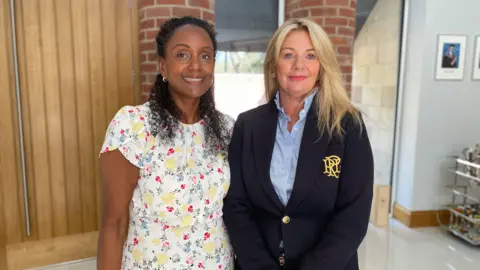 Mark Ansell/BBC Nicola Handley, a black woman with black hair smiles for a photo stood next to Rachel Oakes, who has blonde hair and blue eyes.