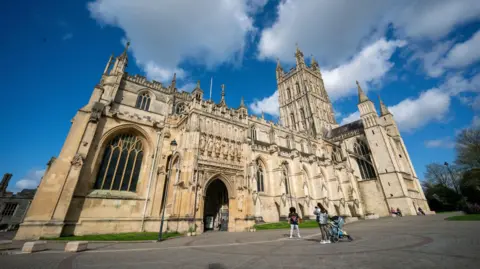 PA Media A cathedral pictured with people standing outside posing for photos under a blue, cloudy sky