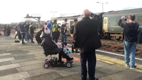 People standing on a platform looking at a train as it passes