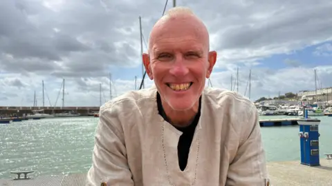 Chrissie Reidy/BBC A man in a white top on a boat.