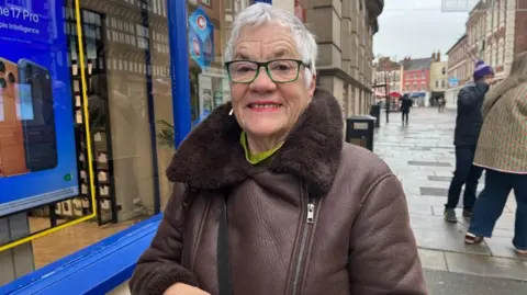 Image of Marilyn in Newark. She is wearing glasses and a maroon jacket.