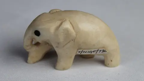 PA Media A small carved piece of ivory in the shape of an elephant with a museum archive sticker on its side